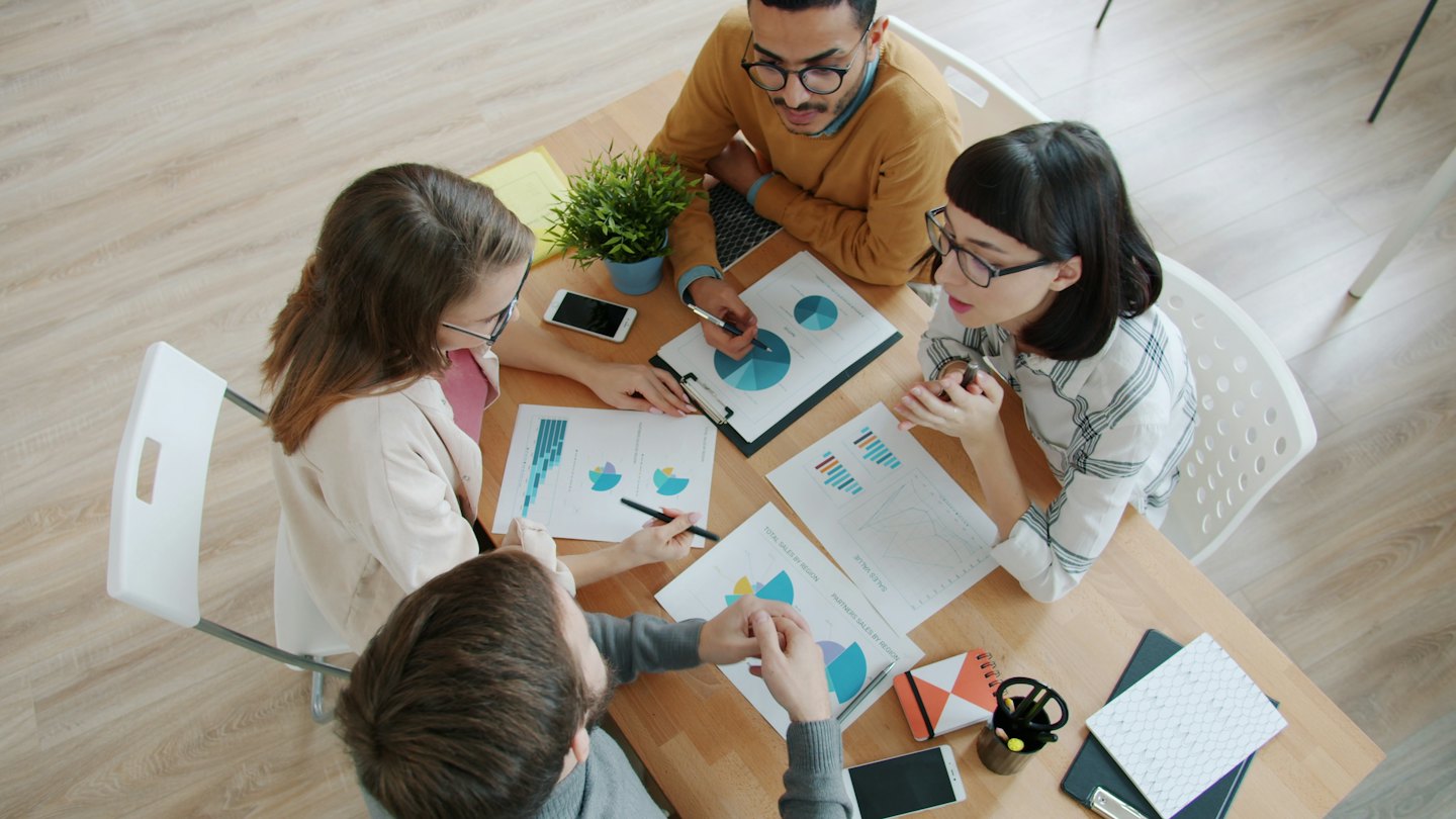 Diverse professionals discuss charts and graphs at a meeting table.
