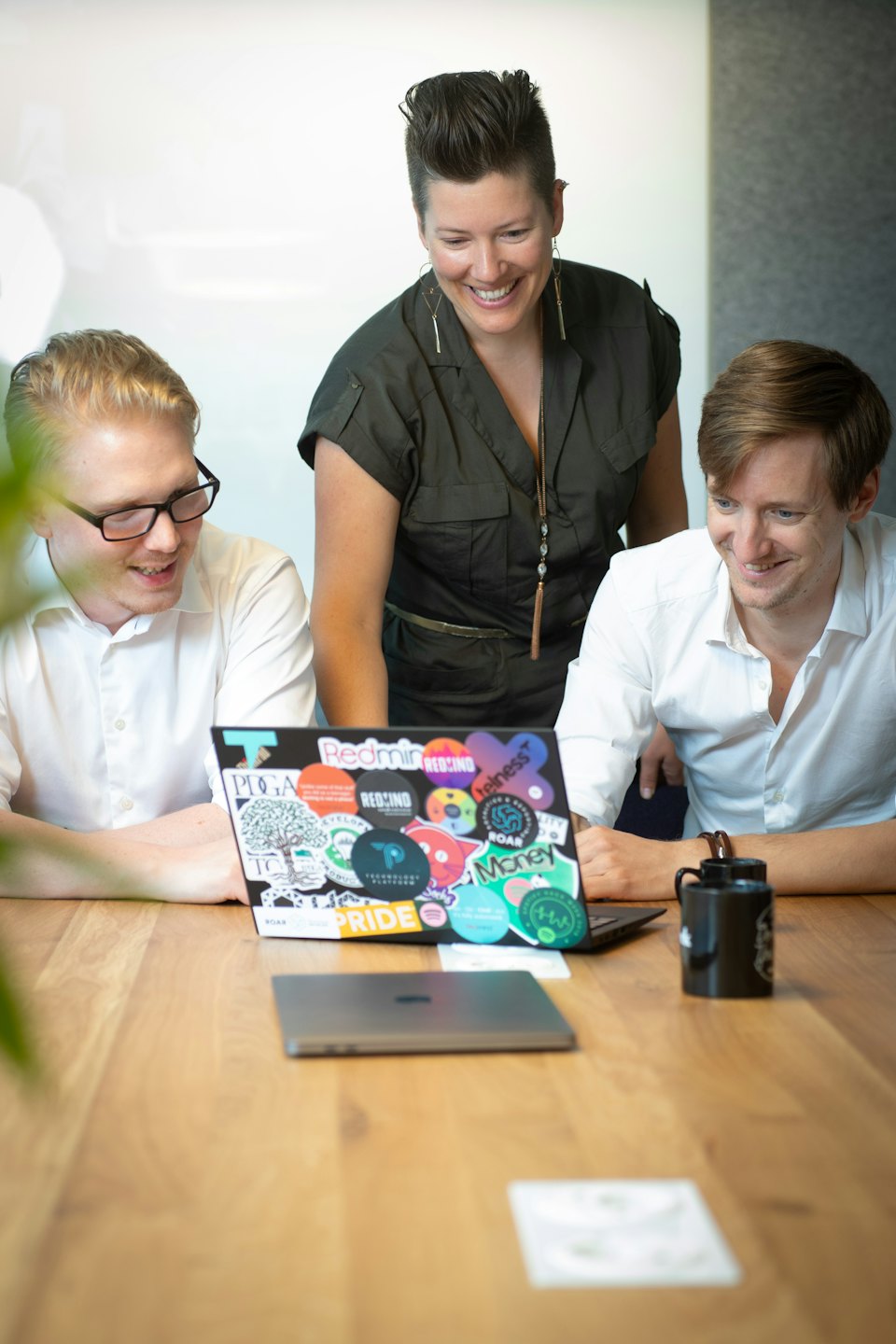 Colleagues smiling while collaborating over a laptop in an office meeting.