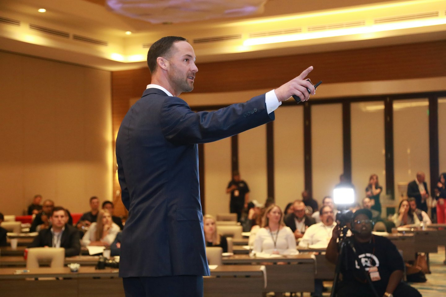 A man in a suit presents to an audience at a conference.